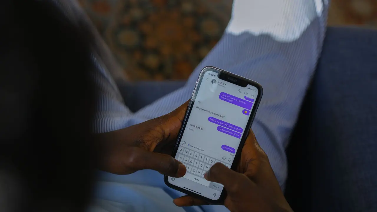 İç mekânda iki eliyle akıllı telefon tutup dokunmatik ekrana yazı yazan bir kişi